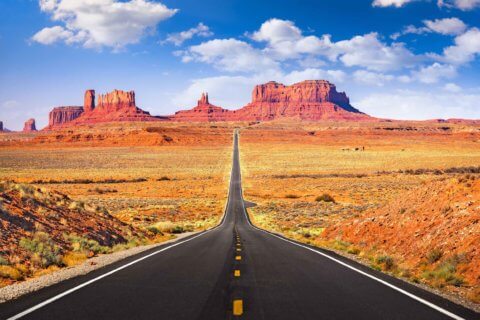 Die lange gerade Straße Monument Valley in der Wüste mit rostroten Sandbergen im Hintergrund.