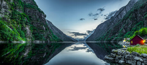 Ein klarer See umhüllt von steilen Felswänden. An der Seite stehen Häuser und ein kleines weißes Boot schwimmt am Ufer.