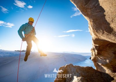 Expeditionsteilnehmer steigt vom Gipfel einer Klippe ab, umgeben von blau schimmerndem Eis